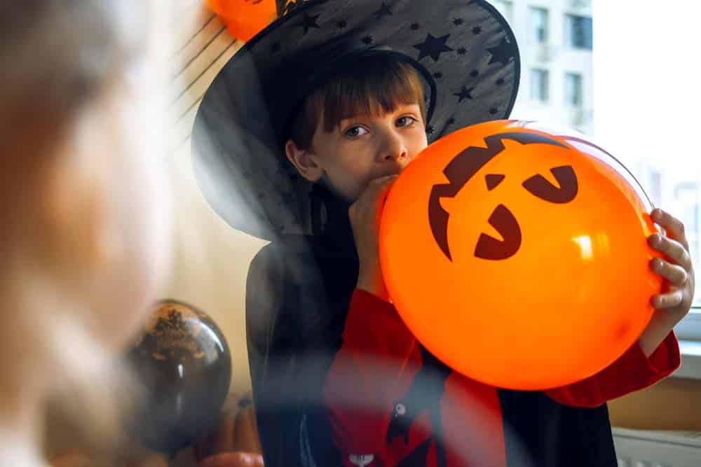 Enfant déguisé en sorcière tenant un ballon citrouille lors d'une fête Halloween