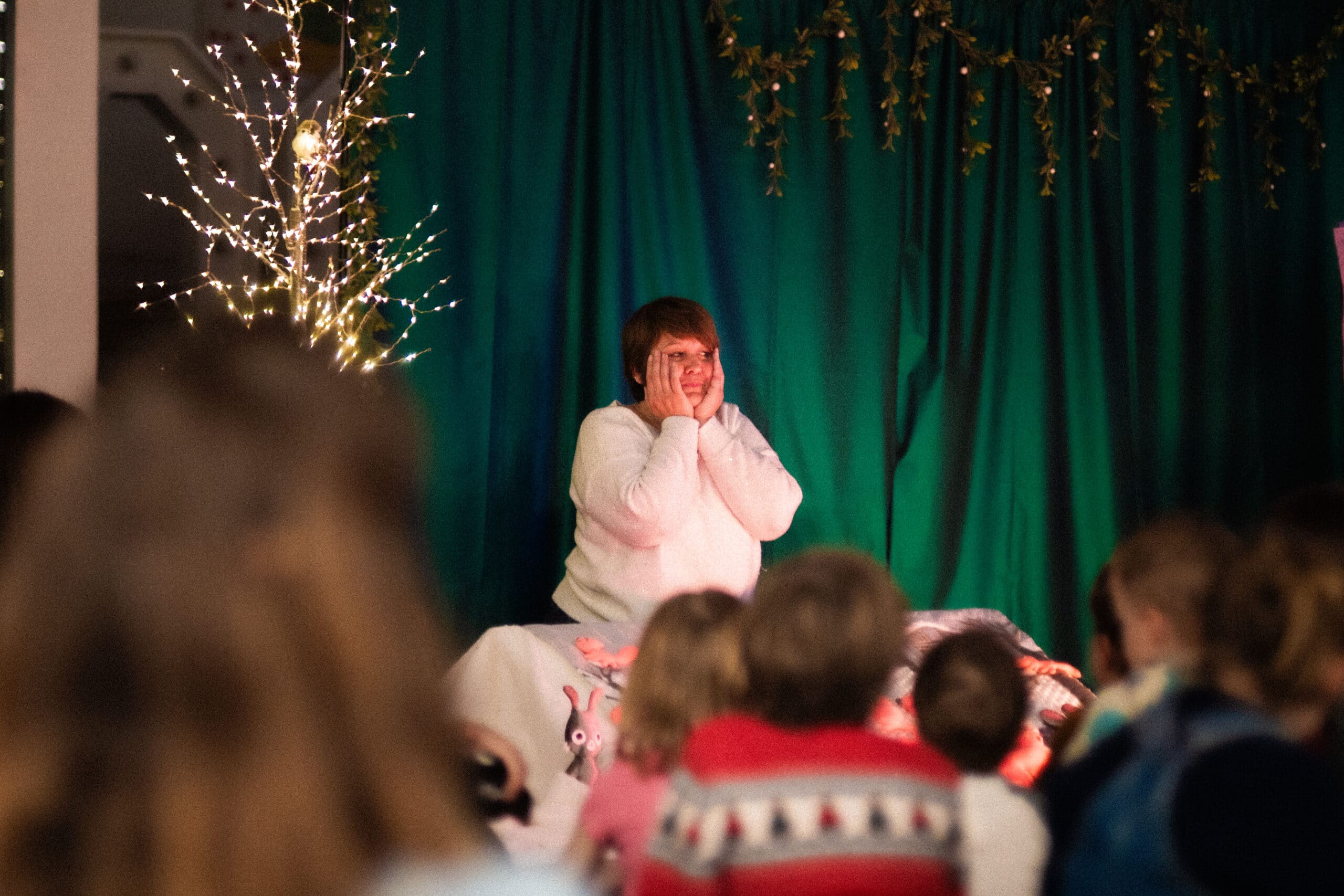 Spectacle de Noël avec conteuse sur scène devant un décor forestier illuminé