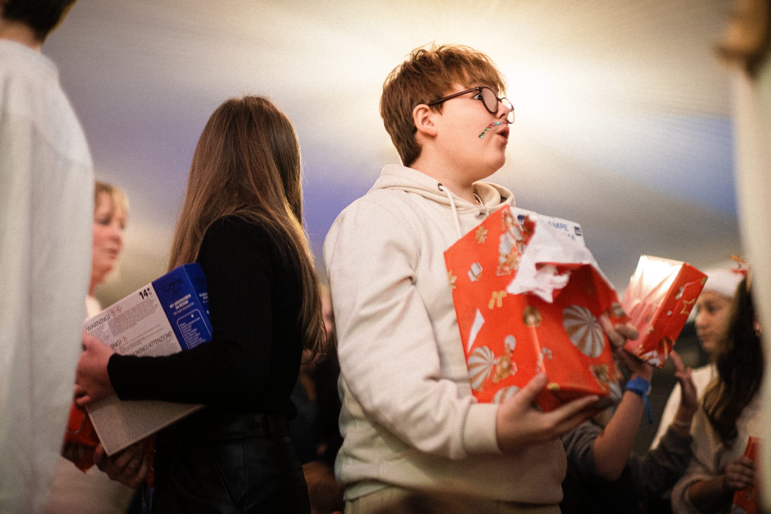 Noël Enfant qui déballe un cadeau de Noël emballé de papier rouge lors d'un arbre de Noël en entreprise